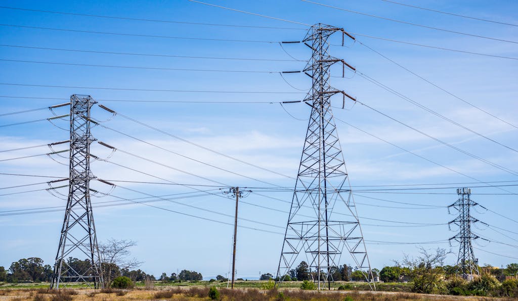 الرئيسية 8 High voltage electric pylons in a field under a clear blue sky demonstrate power transmission infrastructure.