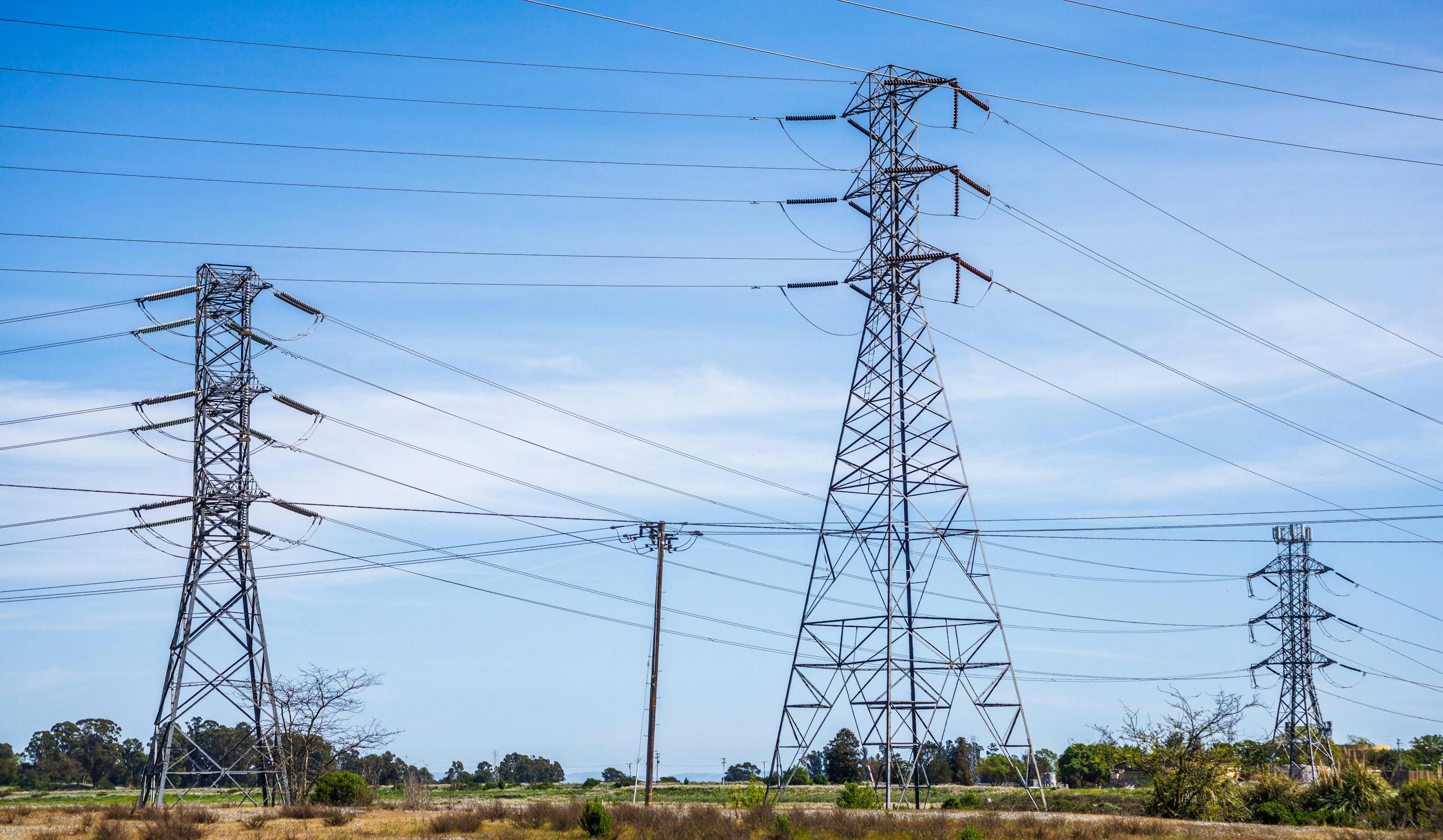 الرئيسية 17 High voltage electric pylons in a field under a clear blue sky demonstrate power transmission infrastructure.